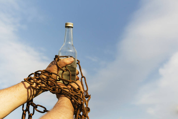 Mano encadenada a una botella de alcohol, contra el cielo azul
 - Foto, imagen