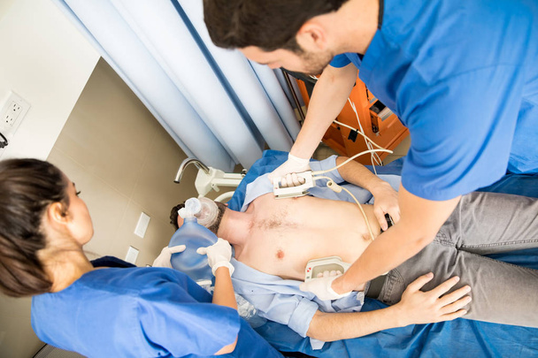 Equipo de paramédicos que realizan tratamiento de RCP con desfibrilador y bolsa ambu en un paciente crítico en sala de emergencias
 - Foto, Imagen