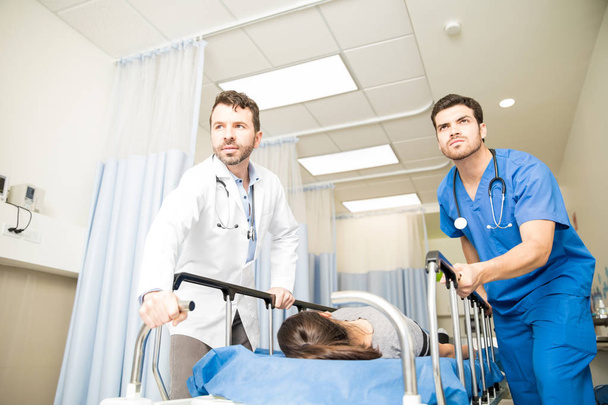 Paar von Ärzten, die während eines Notfalls eine Patientin mit einer Gurney in einen Operationssaal transportieren - Foto, Bild