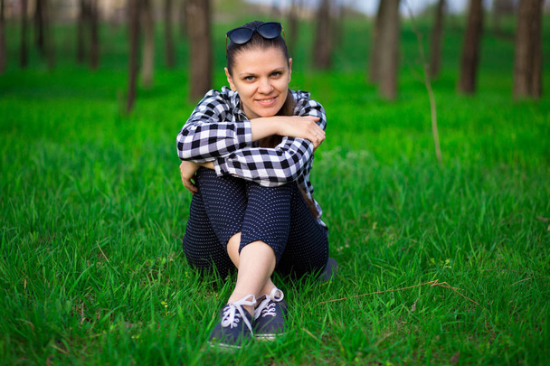 Młody atrakcyjny całkiem kobieta siedzi na trawie odpoczynku przy słonecznej pogodzie w pole na jasne zielone tło. Natura Wiosna. Styl życia, wypoczynek koncepcja - Zdjęcie, obraz