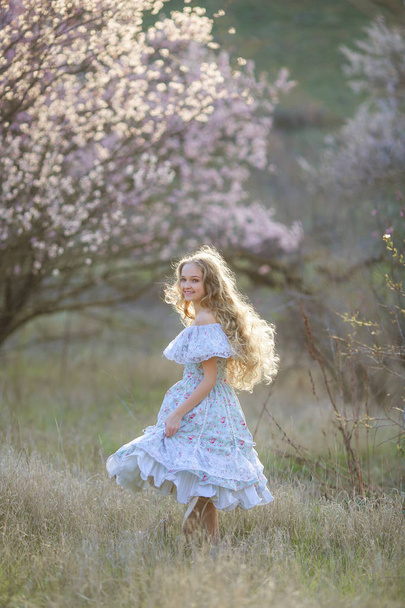 young beautiful blonde girl posing in blossoming garden wearing blue dress  - Foto, Bild