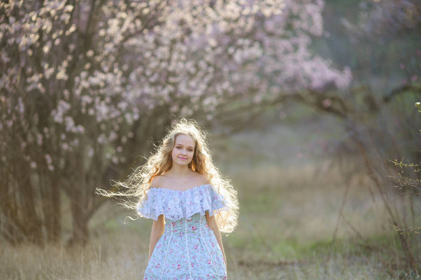 young beautiful blonde girl posing in blossoming garden wearing blue dress  - Фото, изображение