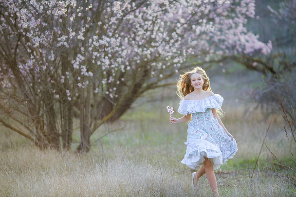 young beautiful blonde girl posing in blossoming garden wearing blue dress  - Φωτογραφία, εικόνα