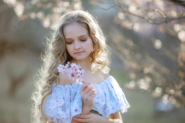 beautiful blonde girl wearing blue dress posing in blossoming garden  - Fotografie, Obrázek