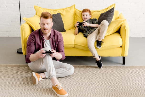 Aus der Vogelperspektive: Vater und Sohn spielen zu Hause gemeinsam mit Joysticks - Foto, Bild
