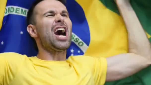 Brasilianischer Fan feiert, während er die brasilianische Fahne in Zeitlupe hält - Filmmaterial, Video