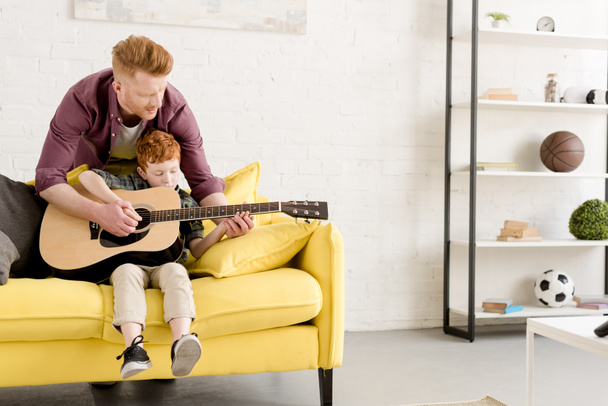 father teaching cute little son playing guitar at home - 写真・画像