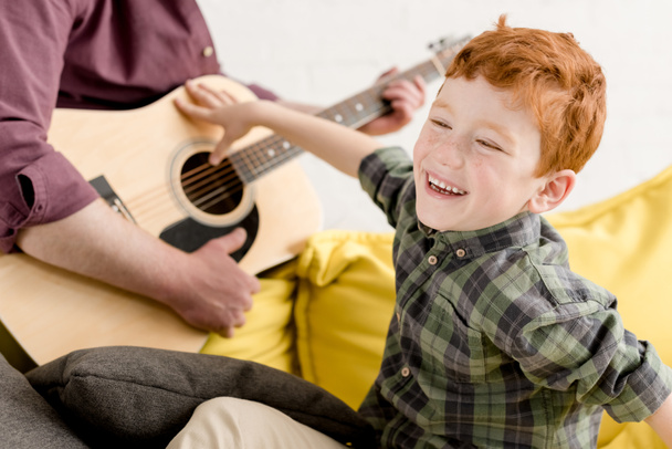 περικοπεί shot του χαριτωμένο μικρό αγόρι γελώντας και παίζοντας κιθάρα του πατέρα - Φωτογραφία, εικόνα