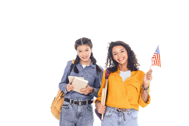 sırt çantaları, kitap ve Amerikan bayrağı üzerinde beyaz izole Interracial öğrencilerle gülümseyen portresi - Fotoğraf, Görsel