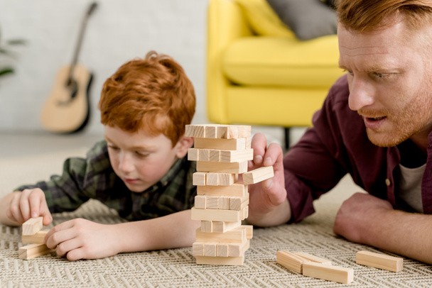 cropped shot of concentrated father and son building towers from wooden blocks at home - Zdjęcie, obraz