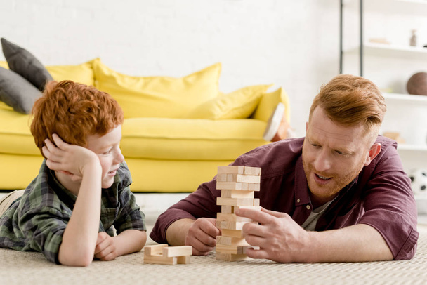 feliz pelirroja padre e hijo jugando con bloques de madera en casa
 - Foto, imagen