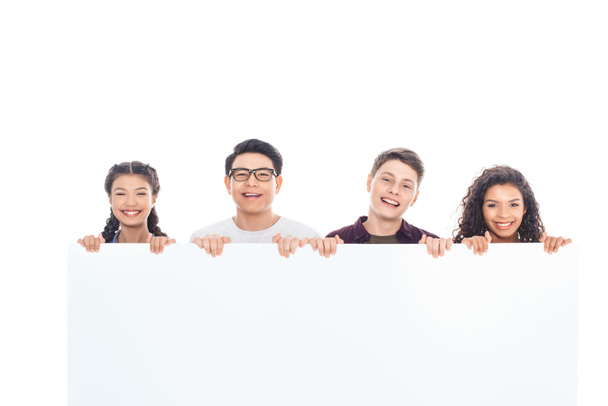 портрет улыбающихся многорасовых подростков, держащих вместе чистый баннер, изолированный на белом
 - Фото, изображение