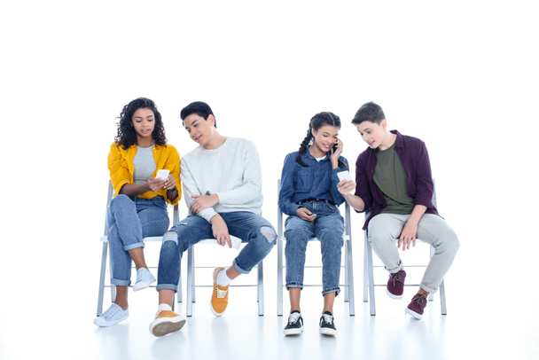 group of teen students using smartphones on chairs isolated on white - Foto, Bild