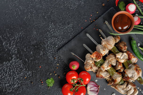 Seductive shish kebabs on a black background.Appetizing meat with fresh vegetables and sauce. - Foto, afbeelding