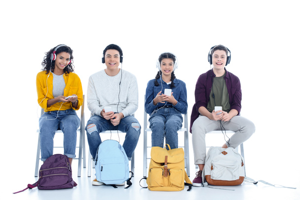 group of teen students in headphones sitting on chairs isolated on white - Foto, Bild