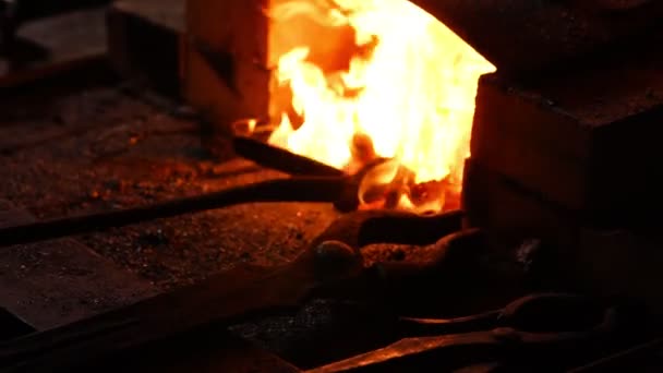 Closeup kováře rozdmýchává plameny pecí, pomocí nástroje zabraňuje uhlíky, jiskry létající na stranu v pomalém pohybu. Detail ruční kovářské. - Záběry, video