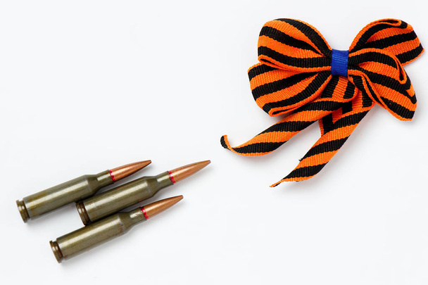eine Schleife aus einem orange-schwarzen St. Georgenband und Patronen, als Symbol, isoliert auf weißem Hintergrund. - Foto, Bild