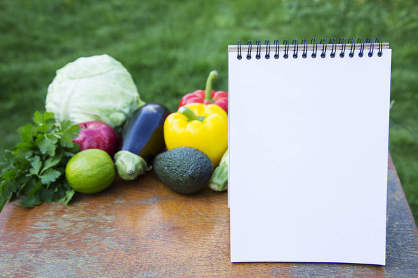Egészséges ételek fogalmát. Notebook és a gyűjtemény a különböző gyümölcsök és zöldségek, a fából készült rusztikus asztal. Oldalnézet. - Fotó, kép