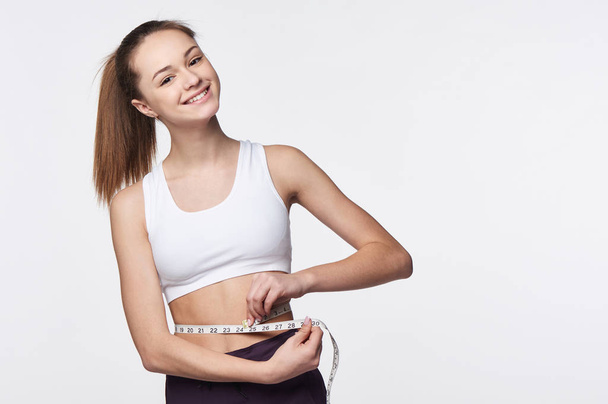 Teen girl measuring her waist with a measuring tape - Φωτογραφία, εικόνα