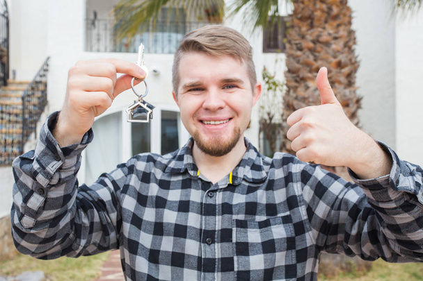 Joven hombre feliz mostrando una llave de la casa y pulgares hacia arriba
. - Foto, Imagen