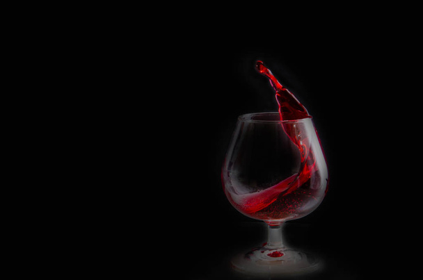Splash of red wine in a glass on a black background - Foto, Imagen