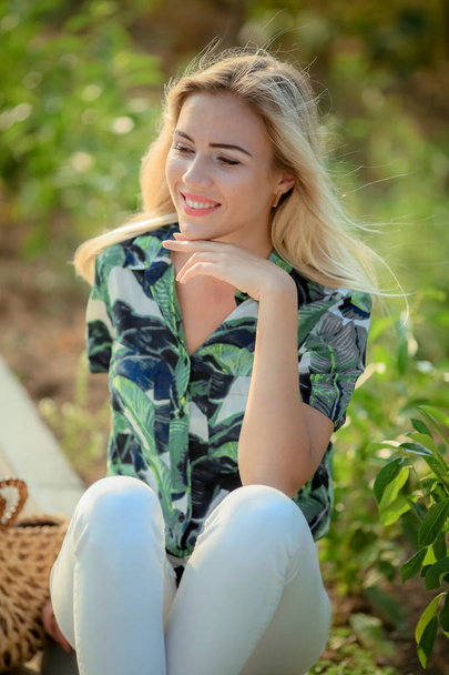 outdoor portrait of beautiful young blonde woman in white trousers and green shirt  - Valokuva, kuva