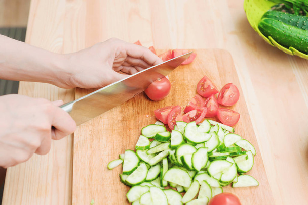 Close-up Delicate female hands cut a large knife with tomatoes on a quarter on a wooden board at home. Home kitchen. Healthy eating. The concept of vegetarianism - Foto, Imagem