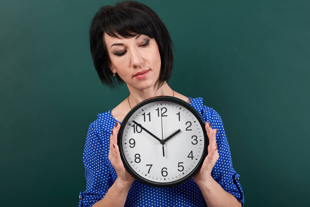 Frau mit großer Uhr posiert mit Kreidetafel, Zeit- und Bildungskonzept, grüner Hintergrund, Studioaufnahme - Foto, Bild