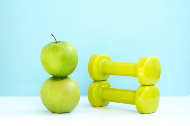 two green apples and dumbbells on blue background - 写真・画像