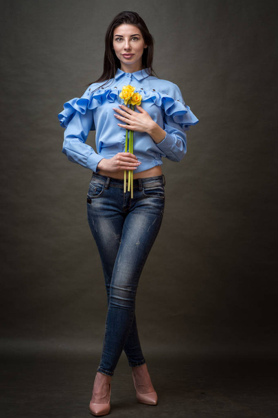 Portrait of a beautiful happy brunette woman in blue shirt holding yellow jonquils in her hands. - Foto, Imagen