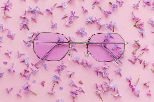 summer vacation and festival concept. stylish purple boho sunglasses on pink background with lilac flowers. creative trendy flat lay with space for text. modern fashion and girly image - Photo, Image