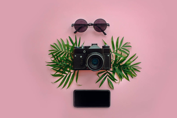 elegáns fekete fényképezőgép zöld Pálma levelek, napszemüveg és a telefon trendi rózsaszín háttér, lapos feküdt. modern csípő utazás kép. nyaralás, hely a szöveg - Fotó, kép