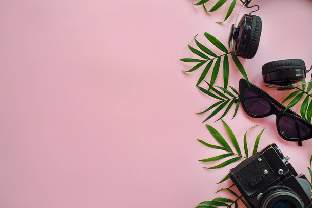 summer vacation flat lay, space for text. stylish black photo camera with green palm leaves, sunglasses and headphones on trendy pink background. modern hipster travel  image. - Фото, изображение