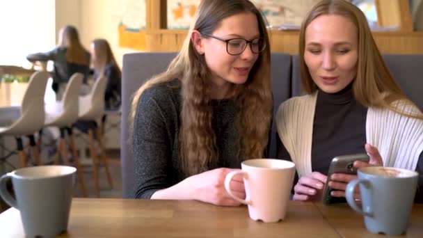 Kaksi ystävää nainen kahvilassa matkapuhelimella ja pitää hauskaa kommunikoida
 - Materiaali, video