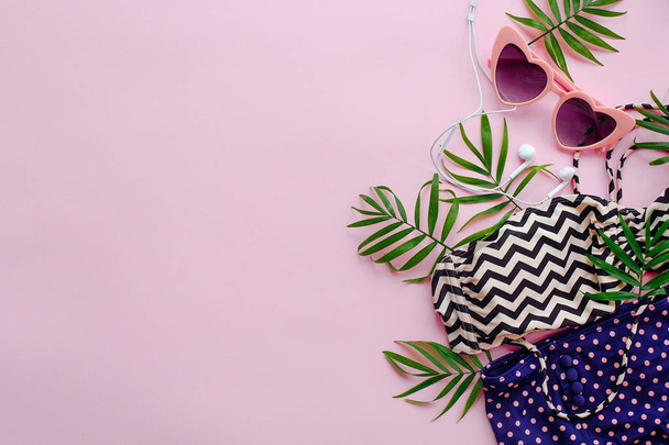 stijlvolle roze zonnebril, moderne badpak, hoofdtelefoons en groene palmbladeren op roze achtergrond, lag plat. ruimte voor tekst. zomer vakantie concept. tijd om te reizen van concept - Foto, afbeelding