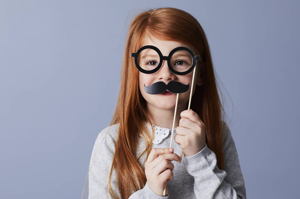 Little redheaded girl in funny disguise with fake mustache and spectacles - Fotoğraf, Görsel