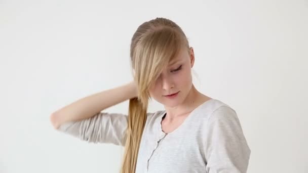 schöne langhaarige Mädchen von europäischem Aussehen mit blonden Haaren machen verschiedene Frisuren auf weißem Hintergrund - Filmmaterial, Video