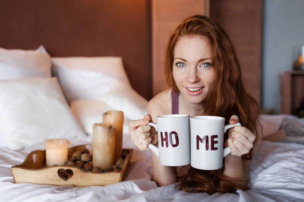 beautiful red haired woman with mugs lying in bed  - Foto, Bild