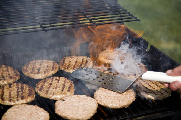 Persoon Flipping hamburgers tijdens BBQ-buiten - Foto, afbeelding