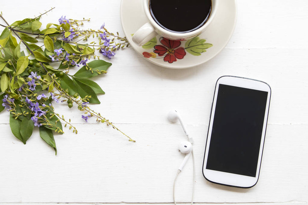 δημοφιλή ποτά hot φρεσκοψημένου καφέ και κινητό τηλέφωνο ακουστικά σε λευκό φόντο - Φωτογραφία, εικόνα