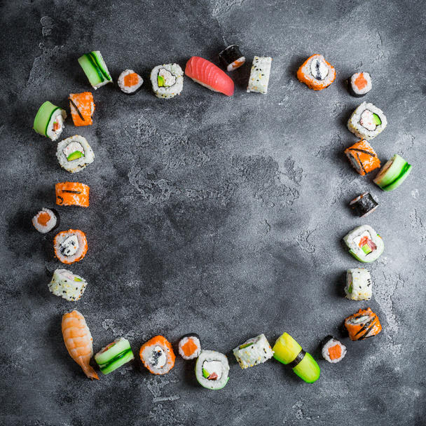 Marco redondo de juego de comida japonesa sobre fondo oscuro. Rollos de sushi, nigiri, filete de salmón, arroz y aguacate. Acostado. Vista superior
 - Foto, Imagen