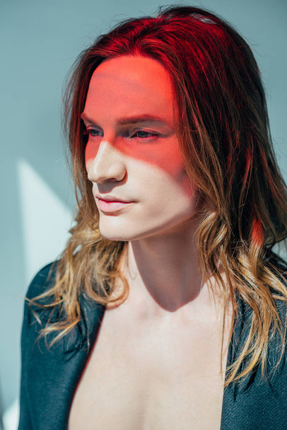 handsome man with long hair and red light on face, on grey - Фото, зображення