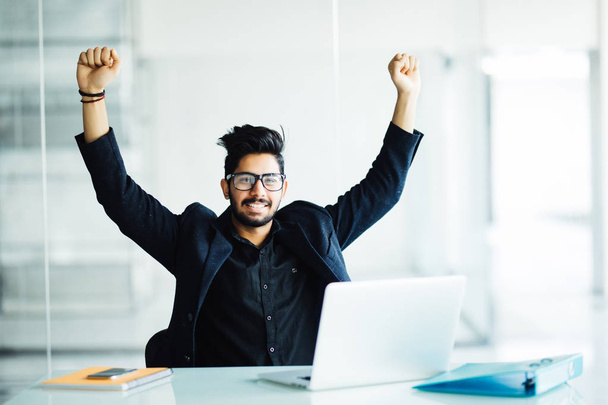 Happy handsome indian businessman in front of laptop at desk in modern office setting celebrating great news, screaming in joy because of victorious achievement. Successful deal, business success conc - Photo, Image