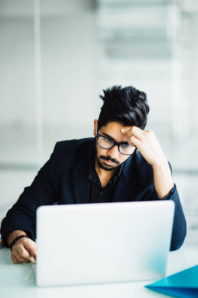 Zdjęcie z Indian Mężczyzna niezadowolony z pracy, siedząc na laptopa w nowoczesnym biurze - Zdjęcie, obraz