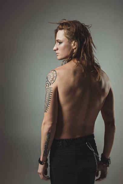 shirtless tattooed man with long hair posing in black jeans, isolated on grey - Foto, afbeelding