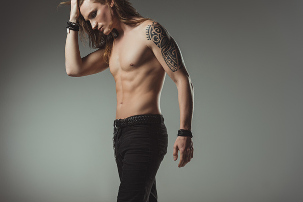 καλαίσθητο shirtless άνθρωπος με τατουάζ που θέτουν σε μαύρο τζιν, απομονώνονται σε γκρι - Φωτογραφία, εικόνα