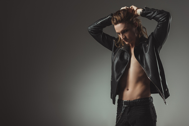 shirtless rocker with long hair posing in black leather jacket, isolated on grey - Fotó, kép