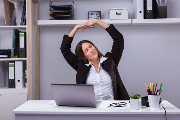 Mature Businesswoman Stretching Her Arms At Workplace - Photo, image