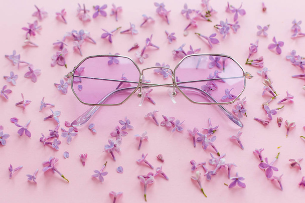 summer vacation and festival concept. stylish purple boho sunglasses on pink background with lilac flowers. creative trendy flat lay with space for text. modern fashion and girly image - Photo, Image