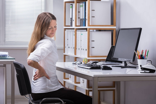Side View Of A Mature Businesswoman Sitting On Chair Suffering From Back Pain - Фото, изображение
